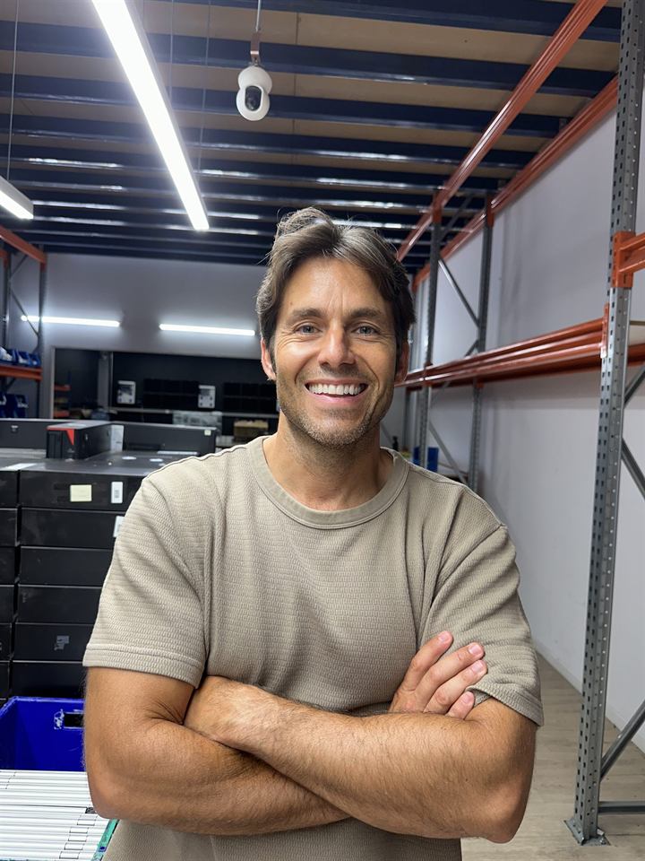 Roberto López, cofundador, de pie y sonriendo en la nave del taller, con estanterías al fondo.